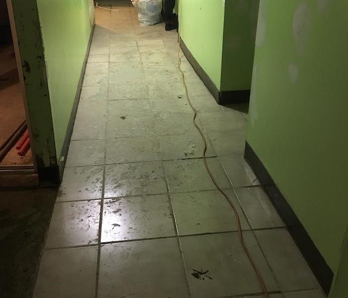 Water on a tile floor with SERVPRO tech in the background