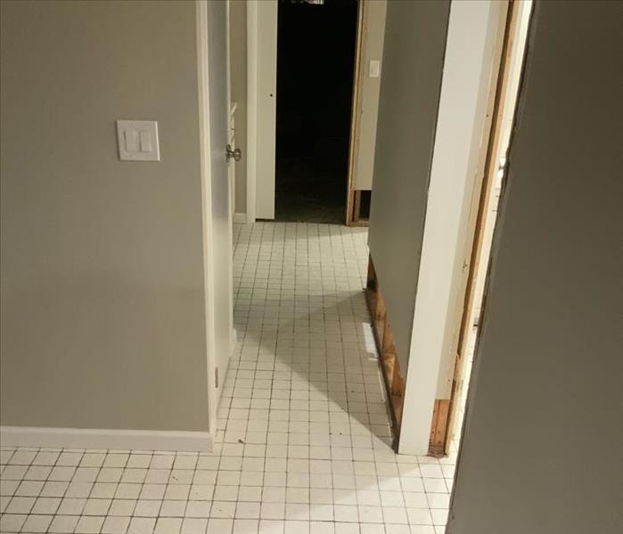 Hallway with white tile floor and removed sheetrock from  the wall