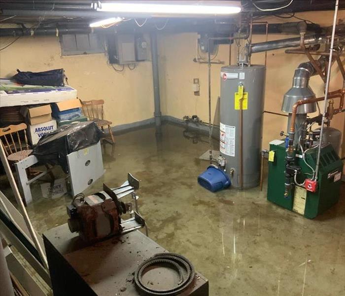 Basement with standing water around furnace and water heater with chairs 