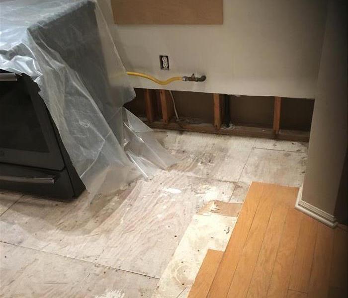 plastic covered oven, cut wall showing studs and removed hardwood planks revealing the plywood sheathing