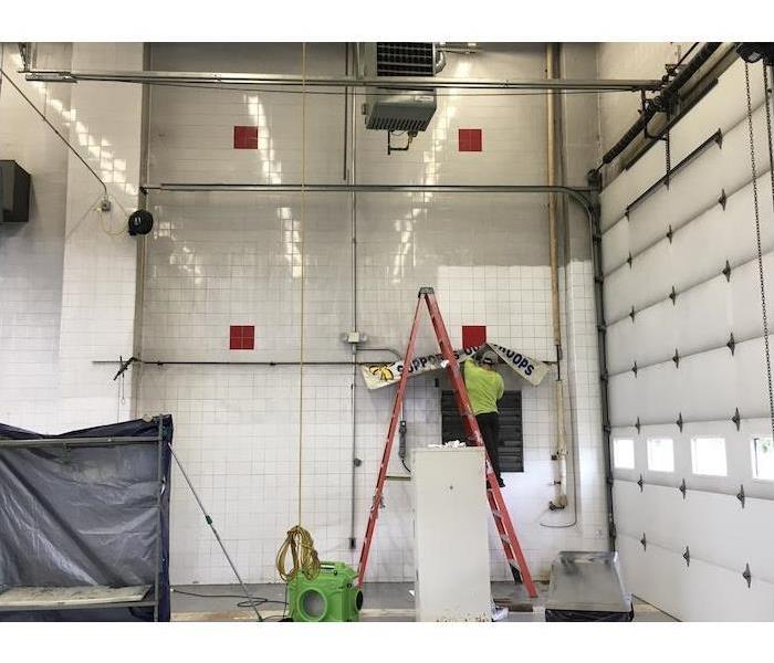 SERVPRO tech on a ladder removing a banner with equipment running at floor level